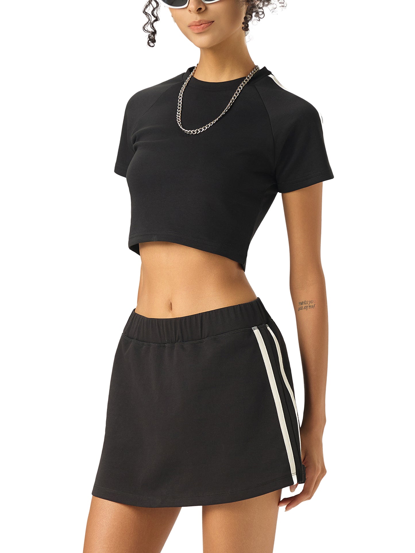 Woman wearing a black crop top and black skirt with white stripes on a white background
