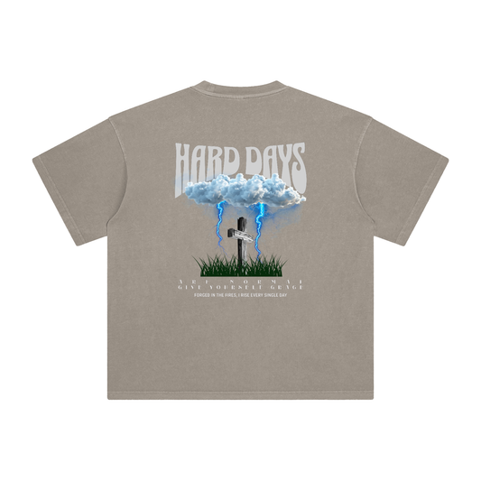 Beige t-shirt with graphic design and text on the back. Graphic design consists of Clouds with lightning, a cross, and some grass graphic. Bold text on the top says "Hard days" and bottom text saying "are normal" "Give yourself grace" "forged in the fires, I rise every single day". 