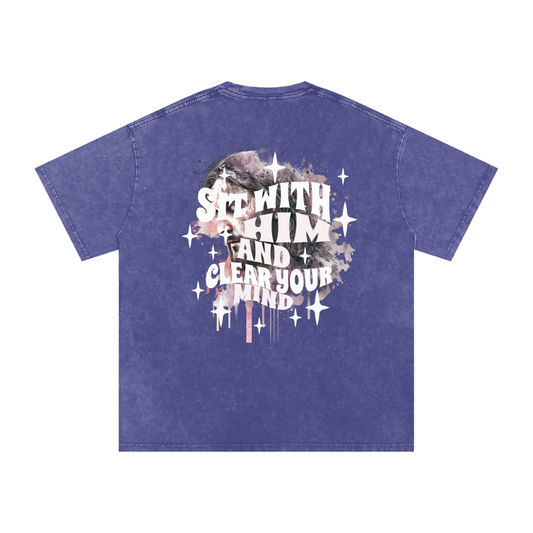 Back of dark purple t-shirt with 'sit with him and clear your mind' text, and a graphic watercolor of Jesus in the colors pink, gray, black, white, and purple, with white sparkles scattered around the design, in front of a white background.
