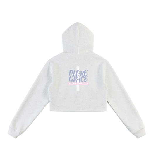Light heather gray cropped zip up hoodie with text and a white cross on the back against a white background. Text says "More grace, less guilt", colors in the design consist of light purple, light pink, and white.