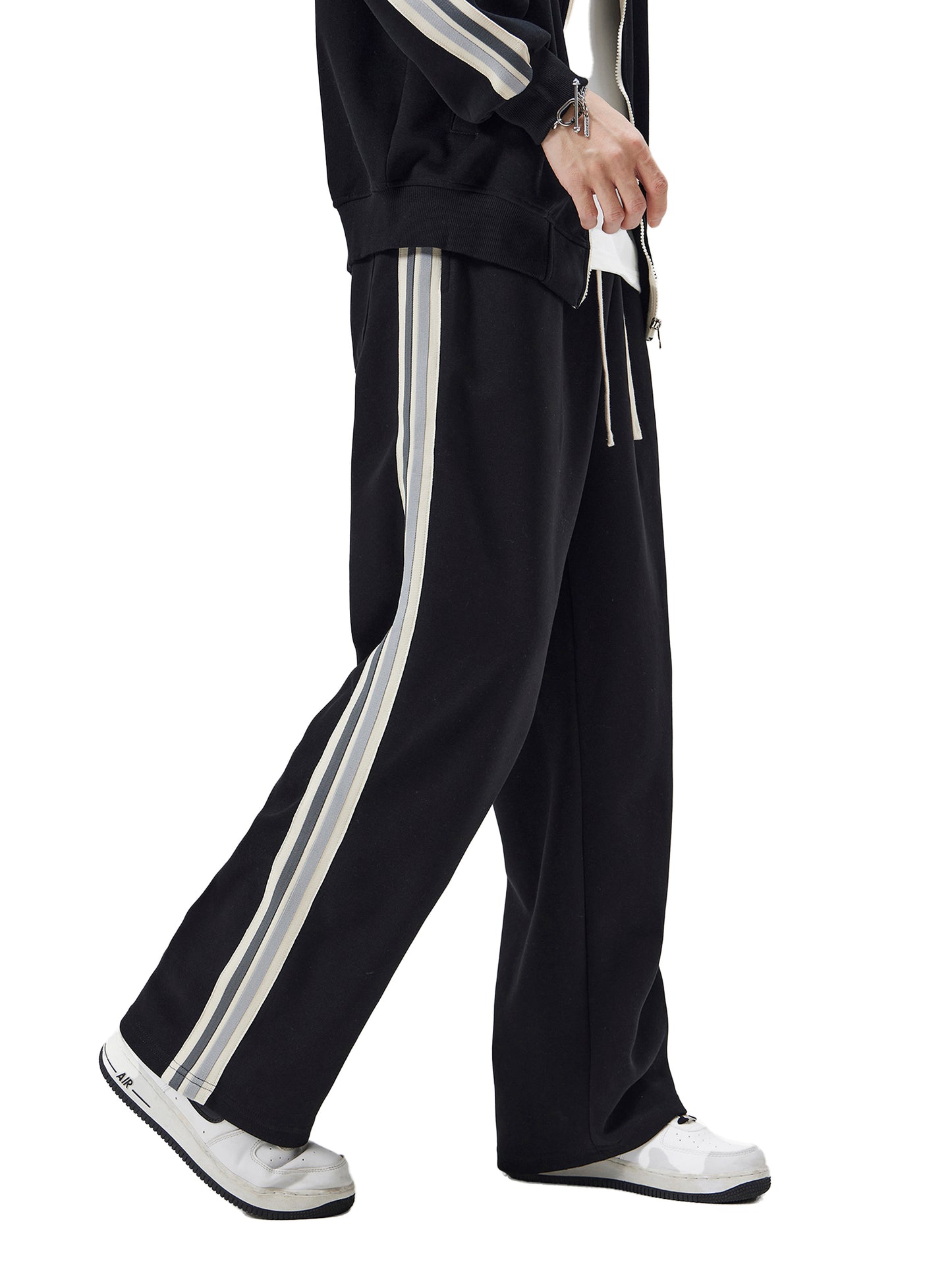 Black tracksuit with white stripes worn by a person on a white background