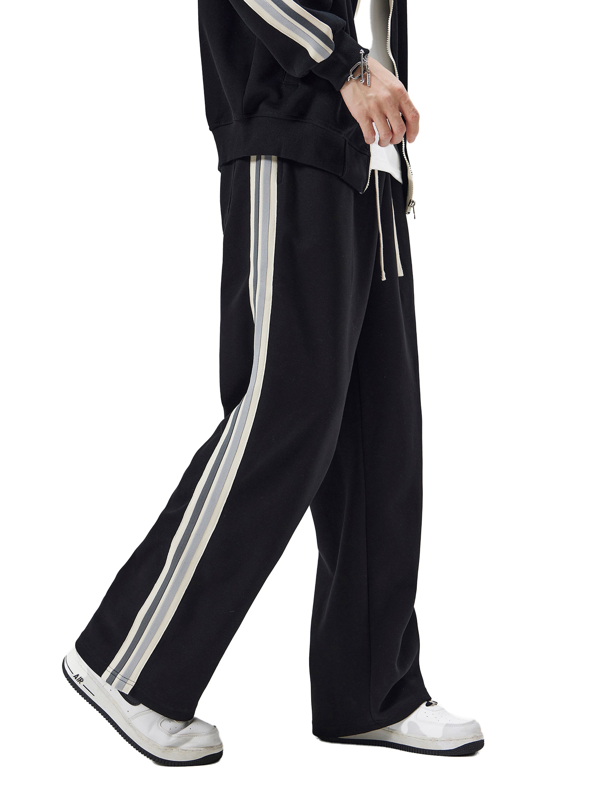 Black tracksuit with white stripes worn by a person on a white background