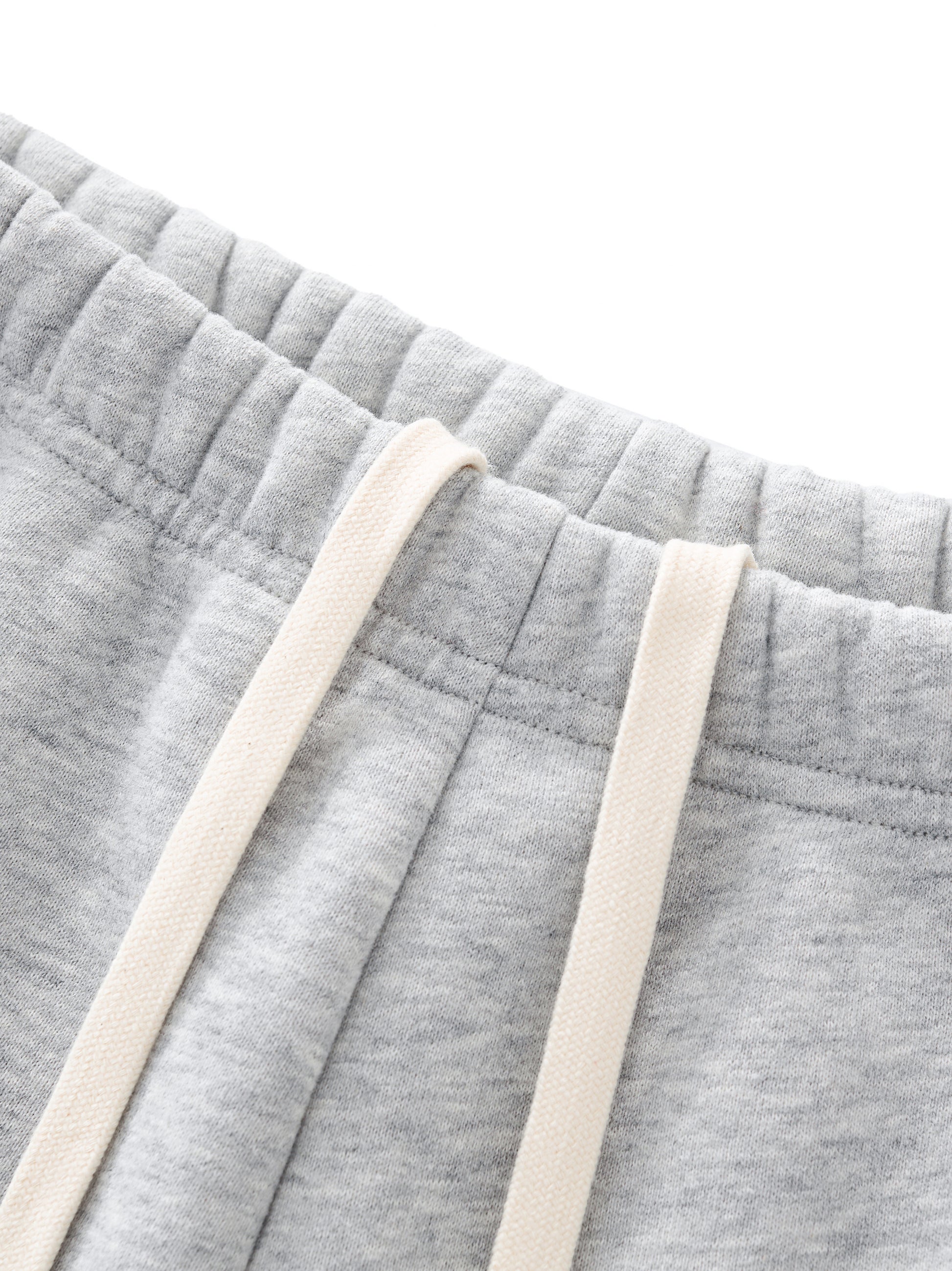 Close-up of gray sweatshorts with beige drawstrings in front of a white background
