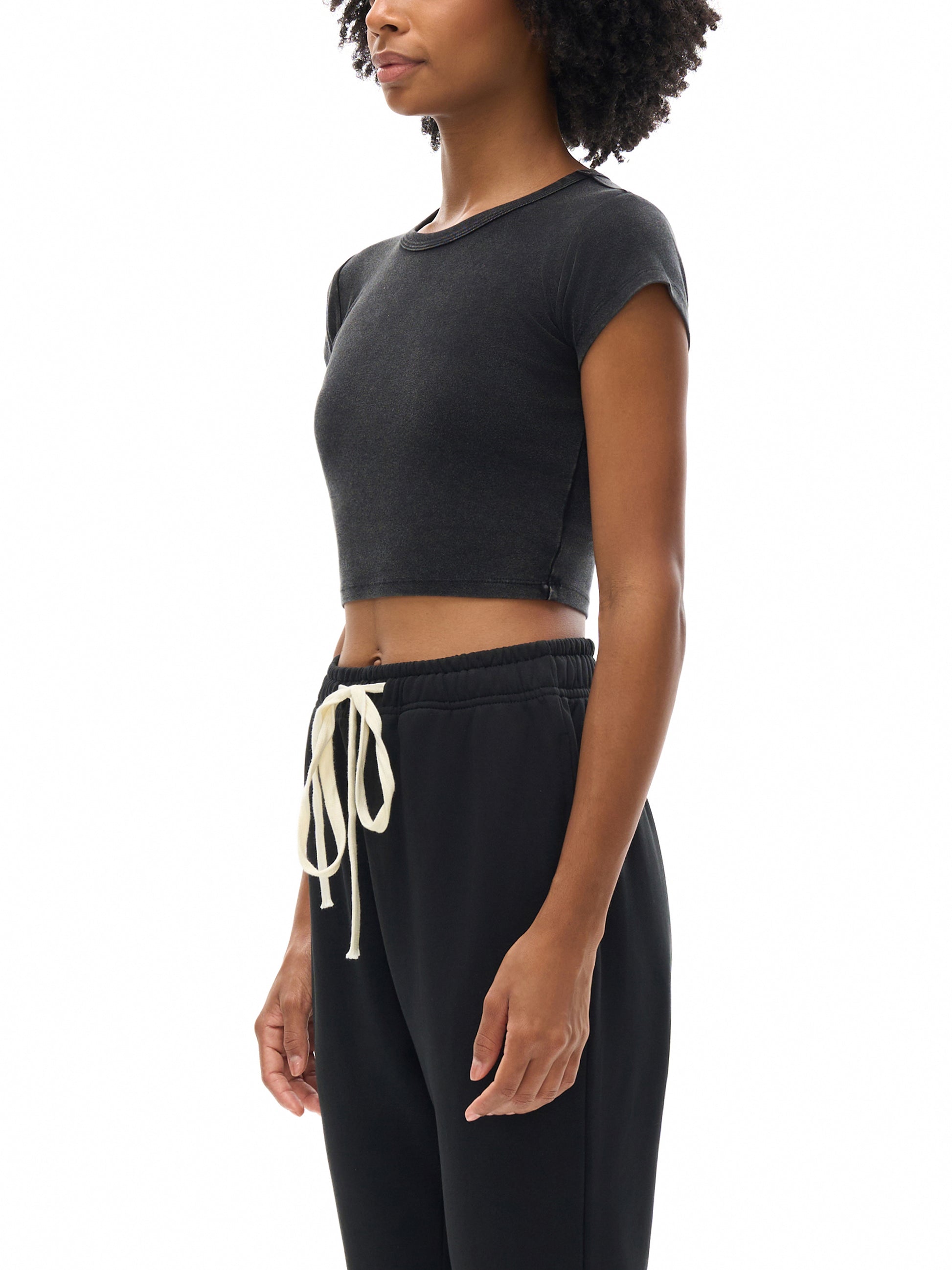 Person wearing a black crop top and black sweatpants with a white drawstring on a white background